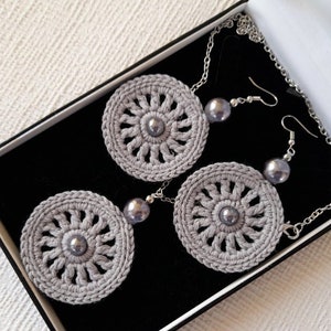 May include: A set of gray crocheted earrings and a necklace with gray crocheted pendants and silver beads.