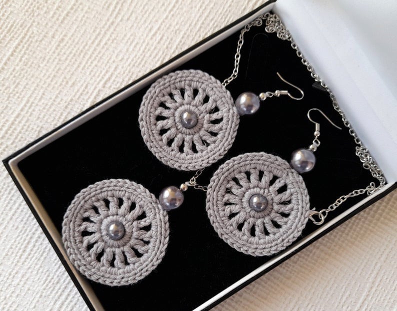 May include: A set of gray crocheted earrings and a necklace with gray crocheted pendants and silver beads.