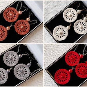 May include: Four pairs of crocheted earrings with pearl accents. The earrings are displayed in black boxes. The colors of the earrings are red, white, gray, and orange.