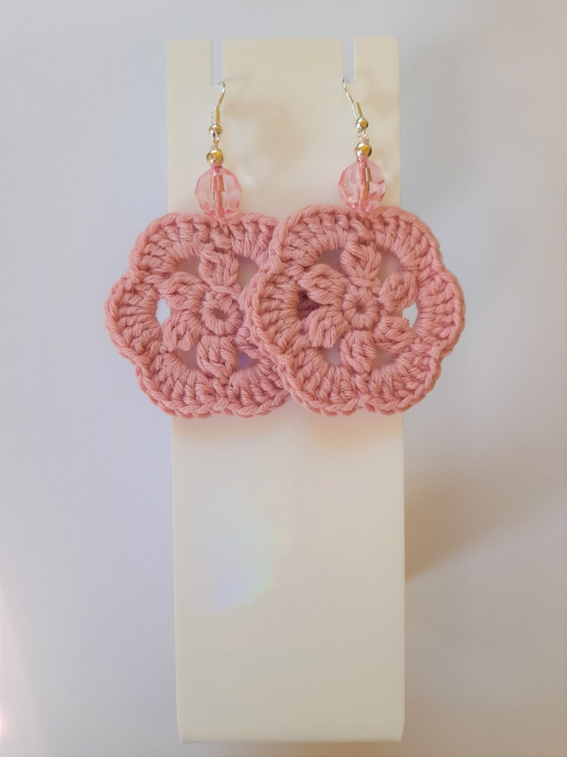 May include: Pink crocheted flower earrings with clear crystal beads hanging from silver hooks.