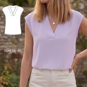 Puede incluir: Una blusa lila con cuello en V y mangas cortas. La blusa se combina con pantalones color crema. La imagen también incluye un dibujo lineal de la blusa y el texto "Tallas 34-46". La modelo lleva collares superpuestos.