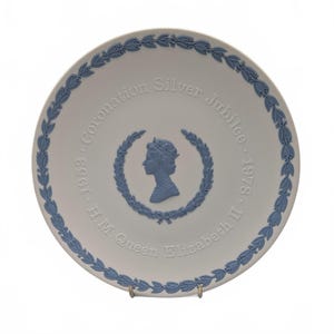 Könnte beinhalten: Ein weißer Gedenkteller mit blauem Blumenrand und zentralem Design. Der Teller zeigt ein Profil von Königin Elisabeth II. in einem Lorbeerkranz mit dem Text "Coronation Silver Jubilee 1953-1978".