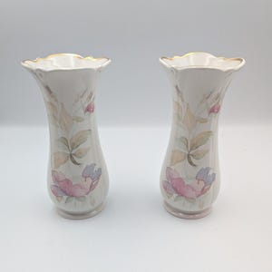 Puede incluir: Dos jarrones de porcelana blanca con borde acampanado y festoneado con un acabado pintado en oro. Cada jarrón muestra un delicado patrón floral estilo acuarela en tonos suaves de rosa, azul y verde apagado sobre un acabado liso y brillante.