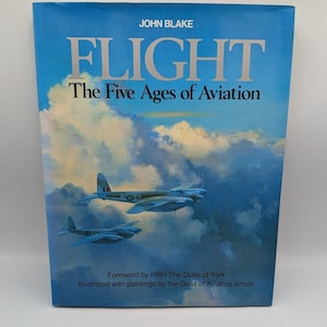 May include: A hardcover book titled FLIGHT The Five Ages of Aviation by John Blake. The cover features a painting of two vintage military aircraft flying through a blue sky with white clouds. It includes a foreword by HRH The Duke of York.