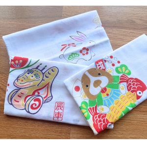 May include: Three white rectangular cotton cloths featuring colourful Japanese-style illustrations. One cloth shows a rabbit, another a gold dragon-like creature with the text 辰車, and the third a brown dog surrounded by red fish and yellow coins.