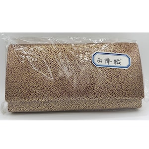 Peut inclure: Une pochette rectangulaire dorée et bordeaux à motifs, scellée dans du plastique transparent. La pochette présente un motif géométrique répétitif. Une petite étiquette blanche et bleue avec du texte japonais est attachée.