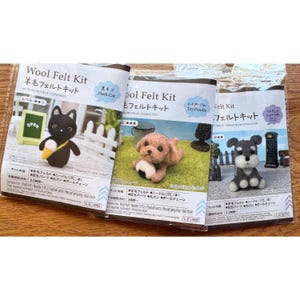 Puede incluir: Tres kits de fieltro de lana en envases de plástico transparente. El kit de la izquierda muestra un gato negro, el central un caniche marrón claro y el de la derecha un schnauzer miniatura gris y blanco. Cada paquete incluye etiquetas de texto.
