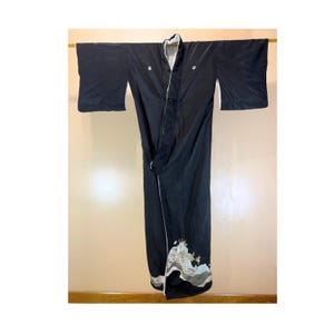 May include: A black kimono with white trim and a decorative landscape design at the hem. The kimono is hanging on a gold rod against a neutral background. The sleeves are wide and the fabric appears to be a lightweight material.