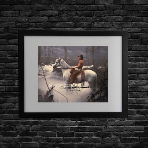 Peut inclure: Une impression encadrée montrant une personne montant un cheval blanc dans une forêt sombre et brumeuse. L'image comporte une signature noire au centre et le texte DO NOT COPY en blanc. L'œuvre est placée dans un cadre noir avec un passe-partout blanc.