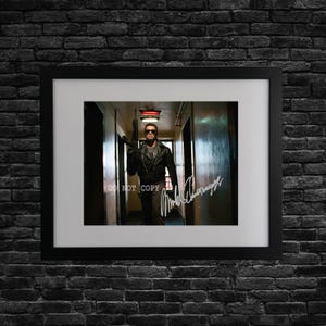 May include: Framed print featuring a man in a black leather jacket and sunglasses, holding a gun. The image is set in a hallway and includes a signature. The words "DO NOT COPY" are visible.