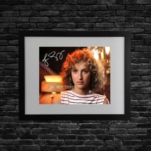 May include: Framed print featuring a woman with curly red hair, wearing a striped top. The image has a signature and the text "DO NOT COPY". The frame is black, set against a dark brick wall.