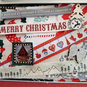 May include: A metal tin filled with assorted fabric scraps and ribbons featuring Christmas themes. Included are ribbons with the text "WITH LOVE AT CHRISTMAS" and "MERRY CHRISTMAS," a wooden tree cutout, a glittery angel wing, and various patterned textiles.