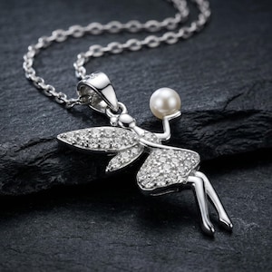 May include: A silver fairy pendant necklace with a delicate design. The fairy figure holds a pearl and is adorned with sparkling crystals on the wings and dress. The necklace chain is also silver, creating a cohesive and elegant piece of jewelry.