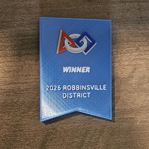 May include: A blue rectangular award with the text "WINNER" and "2026 ROBBINSVILLE DISTRICT". The award has a logo with red, white, and blue accents.