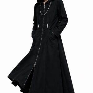 May include: A long black hooded coat featuring a full-length front zipper, two side pockets, and a decorative silver-toned metal chain draped across the chest. The coat has a flared hemline and is worn with black platform boots.
