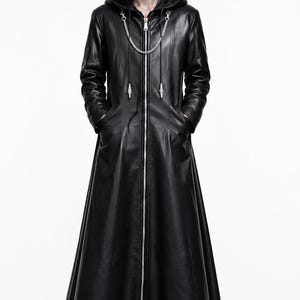 May include: A floor-length black coat with a hood, featuring a full-length silver front zipper, long sleeves, and a decorative silver chain detail across the chest. The coat has a smooth finish and is worn over black shoes, creating a sleek silhouette.