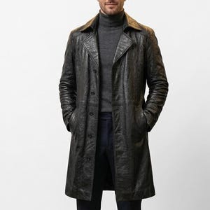 Könnte beinhalten: Ein schwarzer Ledermantel mit strukturierter Oberfläche. Der Mantel hat einen klassischen Kragen, einen Knopfverschluss und Taschen. Die Person trägt einen grauen Rollkragenpullover darunter.