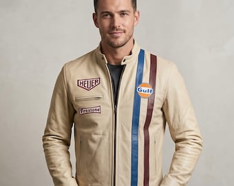 Puede incluir: Chaqueta de cuero color crema con una franja vertical azul y granate. La chaqueta presenta los logotipos de Heuer y Firestone en el pecho y un logotipo de Gulf. Tiene cierre de cremallera y cuello alzado.