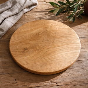 Può includere: Un tagliere circolare in legno con una finitura naturale color marrone chiaro e venature del legno visibili. Il tagliere presenta una superficie liscia e piatta con un bordo arrotondato, che mette in risalto la texture organica e i nodi.