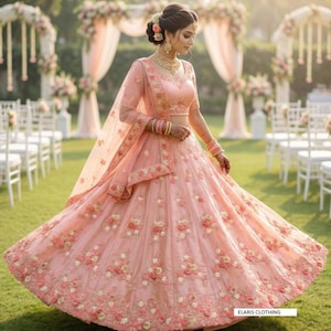 May include: A light peach lehenga with floral embroidery. The outfit includes a matching blouse and dupatta. The image shows a person wearing the lehenga in a garden setting, with a wedding arch and chairs in the background. The text "ELARIS CLOTHING" is visible.