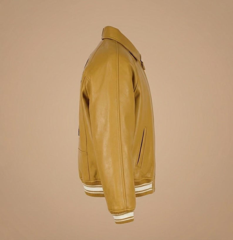 May include: Mustard yellow leather jacket with a classic collar and ribbed cuffs. The jacket features a front zipper and side pockets. The cuffs and hem have white and tan stripes. A stylish outerwear piece.