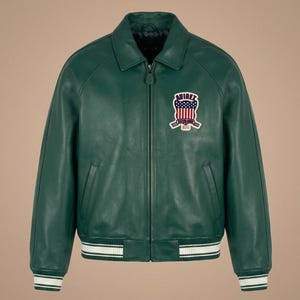 May include: A green leather jacket with a zip-up front, collar, and a patch on the chest. The jacket has white stripes on the cuffs and hem. The patch features a design with red, white, and blue colors.