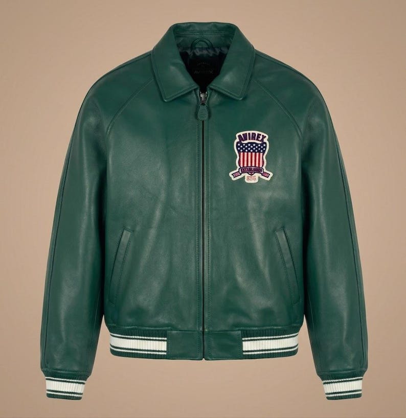 May include: A green leather jacket with a zip-up front, collar, and a patch on the chest. The jacket has white stripes on the cuffs and hem. The patch features a design with red, white, and blue colors.