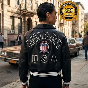 Puede incluir: Chaqueta de cuero negra con letras blancas y un parche con la bandera estadounidense. La chaqueta tiene la palabra "AVIREX", "ALL AMERICANS" y "USA". Rayas blancas adornan los pu&ntilde;os y el dobladillo. Estilo bomber cl&aacute;sico.