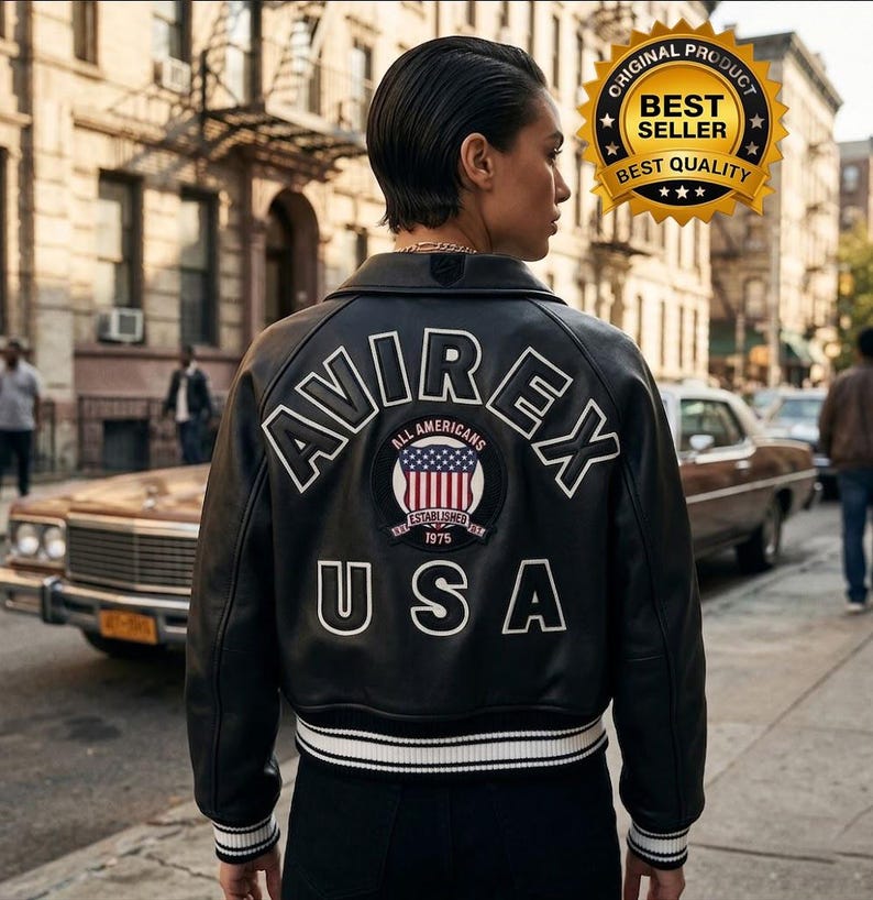 Puede incluir: Chaqueta de cuero negra con letras blancas y un parche con la bandera estadounidense. La chaqueta tiene la palabra "AVIREX", "ALL AMERICANS" y "USA". Rayas blancas adornan los pu&ntilde;os y el dobladillo. Estilo bomber cl&aacute;sico.