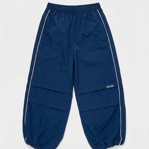 May include: Navy blue athletic pants featuring an elastic waistband, white piping along the side seams, and horizontal paneling across the thighs. The word SWIM is printed in white on the right thigh, and the leg openings have elastic cuffs.