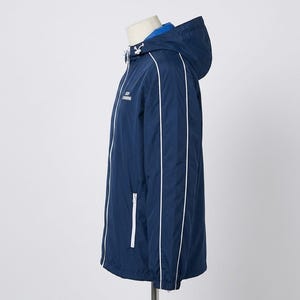 May include: A navy blue windbreaker jacket featuring a hood with white drawstrings, a bright blue inner lining, and white piping along the sleeves. The jacket includes a white zippered pocket on the front and white text on the chest area.