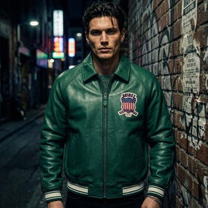 May include: A green leather jacket with a zip-up front and a collar. The jacket has a patch on the chest with the text "AVIREX" and a design of red and blue stripes and stars. The jacket has white stripes on the cuffs and the bottom hem.