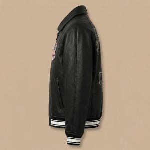 K&ouml;nnte beinhalten: Eine schwarze Leder-Collegejacke mit klassischem Kragen, langen &Auml;rmeln und einem Frontrei&szlig;verschluss. Die Jacke verf&uuml;gt &uuml;ber einen farbenfrohen gestickten Aufn&auml;her auf der Brust und wei&szlig;e Stickbuchstaben auf der R&uuml;ckseite sowie gestreifte Rippb&uuml;ndchen an &Auml;rmeln und Saum.