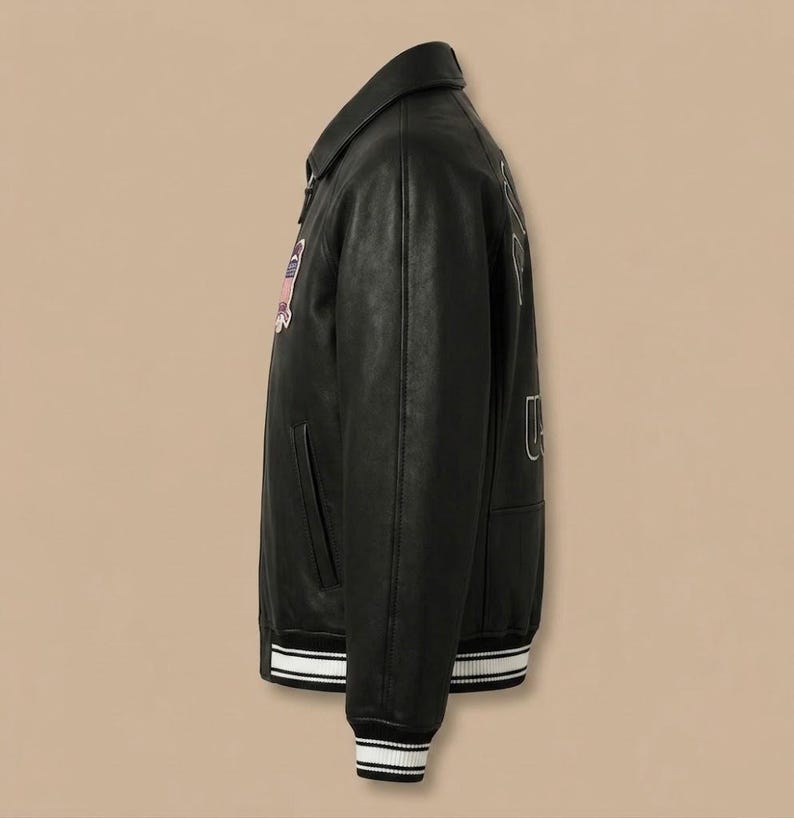 K&ouml;nnte beinhalten: Eine schwarze Leder-Collegejacke mit klassischem Kragen, langen &Auml;rmeln und einem Frontrei&szlig;verschluss. Die Jacke verf&uuml;gt &uuml;ber einen farbenfrohen gestickten Aufn&auml;her auf der Brust und wei&szlig;e Stickbuchstaben auf der R&uuml;ckseite sowie gestreifte Rippb&uuml;ndchen an &Auml;rmeln und Saum.