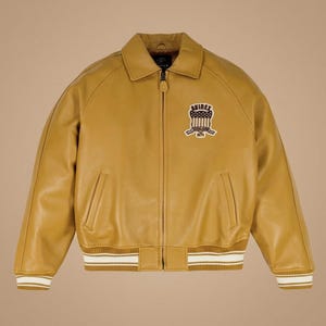 May include: Mustard yellow leather jacket with a zip closure, collar, and ribbed cuffs and hem. Features a patch on the chest with the text "AVIREX 1975". The jacket has two front pockets and a classic bomber jacket design.