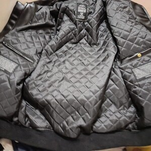 May include: Black leather jacket with a quilted, diamond-patterned lining. The jacket features a ribbed collar and cuffs, and a label is visible on the inside. The jacket has two pockets and a zipper closure.