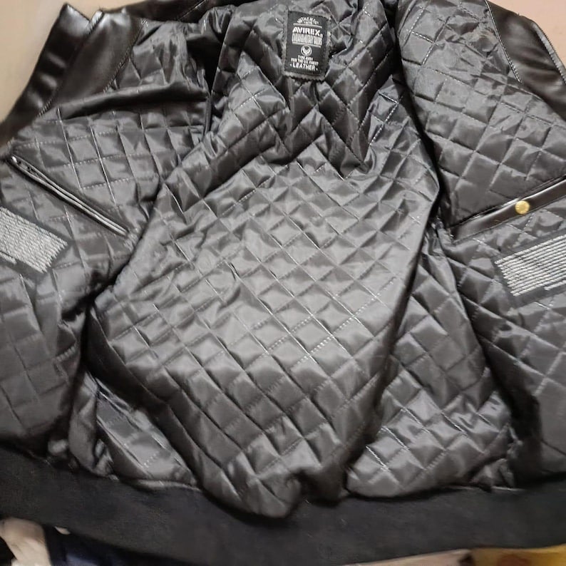 May include: Black leather jacket with a quilted, diamond-patterned lining. The jacket features a ribbed collar and cuffs, and a label is visible on the inside. The jacket has two pockets and a zipper closure.