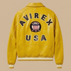 May include: A mustard yellow leather varsity jacket featuring the text AVIREX in black letters arched across the upper back. A circular patch displays an American flag emblem with the text ALL AMERICANS ESTABLISHED 1975. The word USA appears below.