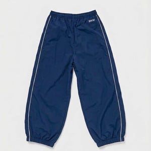 May include: Navy blue athletic pants featuring an elastic waistband and cuffs. The pants have a white vertical piping detail running down the outer legs and the word SWIM printed in white text on the upper right side near the waistband.