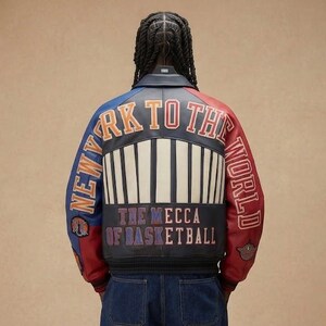 May include: A leather jacket with a color block design in blue, red, and black. The back of the jacket features the text "NEW YORK TO THE WORLD" and "THE MECCA OF BASKETBALL". The jacket has a ribbed design.