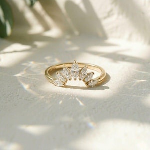 May include: A gold ring featuring a curved band set with seven marquise-cut clear stones arranged in a fan-like pattern. The band is stamped with 14k gold markings. The design creates a crown-like shape with the stones tapering in size.