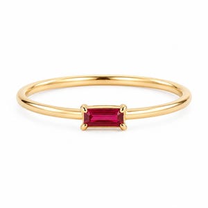 May include: A delicate gold ring featuring a rectangular, vibrant red gemstone. The ring's band is thin and polished, with the gemstone securely set in a four-prong setting. The ring is a piece of fine jewelry.