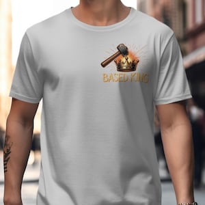 May include: A light gray t-shirt featuring a graphic of a hammer, crown, and the words "BASED KING" in gold. The design includes a burst of orange and yellow radiating from behind the crown.