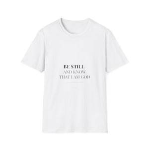 Könnte beinhalten: Weißes T-Shirt mit dem schwarzen Text "BE STILL AND KNOW THAT I AM GOD". Das T-Shirt hat kurze Ärmel und einen Rundhalsausschnitt. Der Text ist mittig auf der Vorderseite des Shirts platziert.