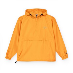 Könnte beinhalten: Eine leuchtend orangefarbene Anorakjacke mit Kapuze und halbem Reißverschluss. Die Jacke hat eine Vordertasche und ein kleines Logo auf der Brust. Die Ärmel haben elastische Bündchen und der Saum einen Kordelzug. Das Champion-Logo befindet sich auf dem Ärmel.