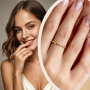May include: A gold ring featuring the name "Grace" in a cursive script. The ring is displayed on a finger, with a close-up view emphasizing the elegant design and the polished finish of the jewellery. The ring is a simple yet stylish accessory.
