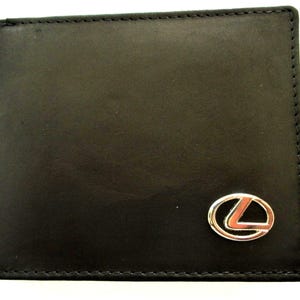 May include: A black bi-fold wallet featuring a smooth texture and visible stitching along the edges. A silver-toned metal emblem shaped like the letter L inside an oval is attached to the bottom right corner of the front exterior surface.