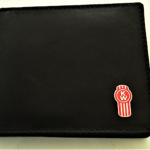May include: A black bi-fold wallet featuring a smooth, matte finish and visible stitching along the edges. Attached to the lower right corner is a small, vertical, red and white emblem with the letters KW centered inside a circular top section.