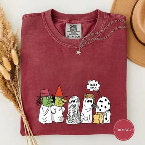 May include: A crimson short-sleeve t-shirt featuring a graphic of five characters dressed in white ghost costumes. One character holds a brown bag and a speech bubble with the text I GOT A ROCK. The shirt has a crew neckline and a Comfort Colors label.