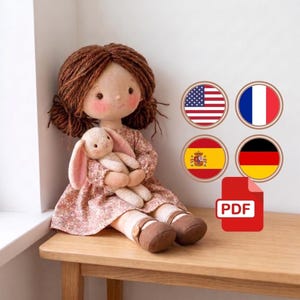 May include: A fabric doll with brown yarn hair styled in pigtails, wearing a floral print dress and brown shoes, holding a small cream-colored plush rabbit. Four circular flag icons and a red PDF icon are positioned to the right.